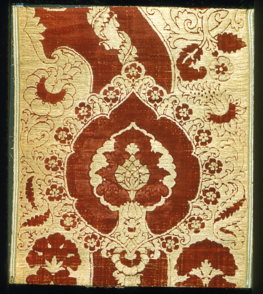 Cream-colored weaving featuring a floral motif in reddish brown, one main flower in the middle with others surrounding it.