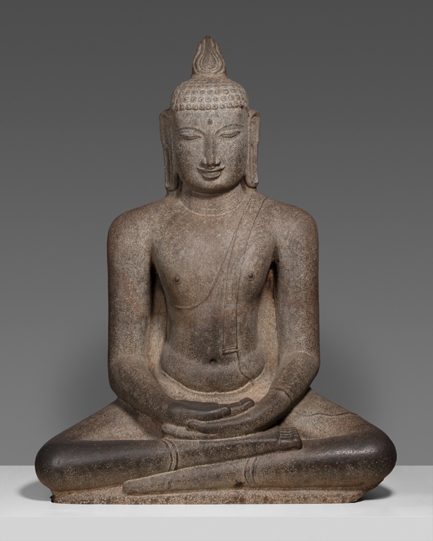 Dark stone sculpture of Buddha sitting cross-legged, hands in lap, eyes closed.