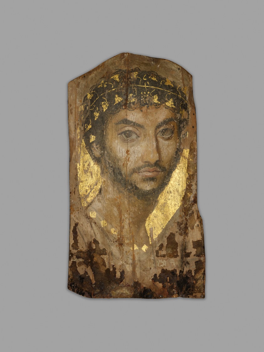 A portrait of a young man with dark hair and beard painted on an irregular piece of wood. The background is gold as a wreath of ivy and necklace he wears. There are many areas where the paint has come off the surface.