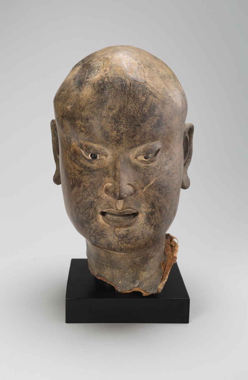 Sculpture of Asian man’s head, he is bald with detailed angular facial features.