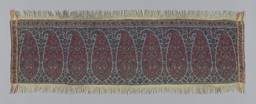 Tapestry with paisley design throughout in reds, purples, blues, and beiges, with fringe on top and bottom.