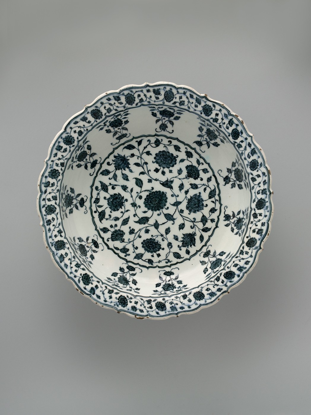A blue-and-white dish viewed from above, with a scalloped rim and floral scrolls.