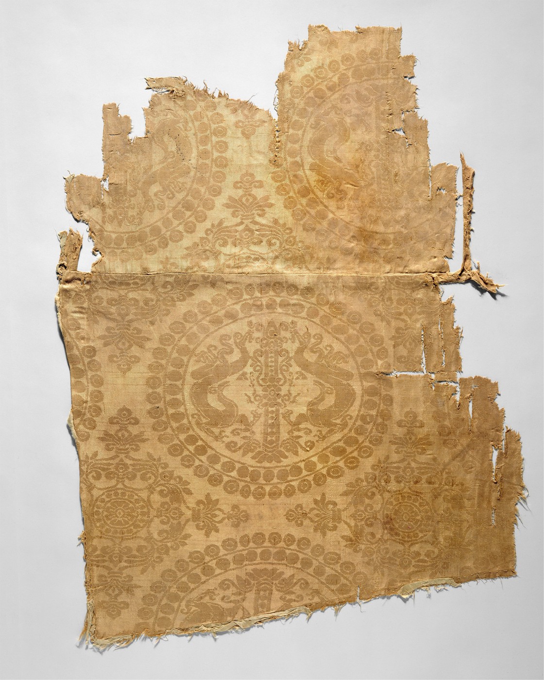 A silk fragment with repeated pearl-bordered roundels enclosing paired curling dragons.