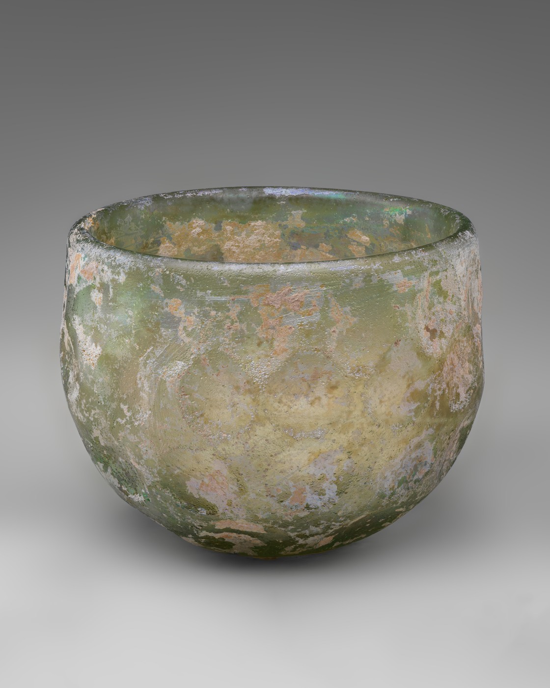 A rounded greenish glass bowl with pale patches across a weathered, iridescent surface.